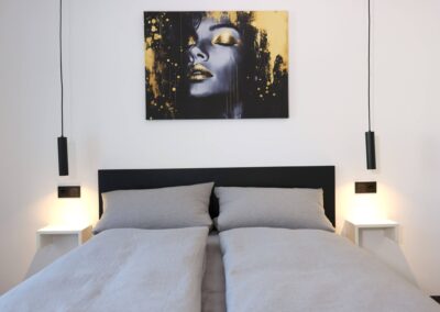 Modernes Doppelbett im Schlafzimmer der Ferienwohnung Petra in Ilmenau mit Pendelleuchten und Kunstwerk