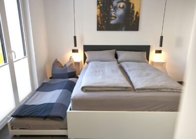 Helles Schlafzimmer mit komfortablem Doppelbett, der Aufbettung für dritte Person und moderner Wandkunst in der Ferienwohnung Petra in Ilmenau, Thüringer Wald
