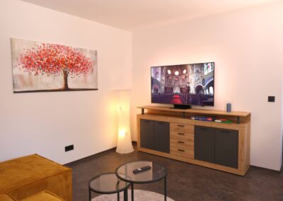 Modernes Wohnzimmer der Ferienwohnung Petra in Ilmenau mit Fernseher, Glastischen und farbigem Wandbild